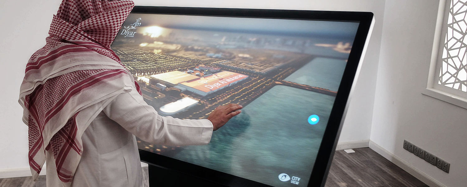 A client operating a large-format CityView touchscreen, exploring an illuminated coastal masterplan